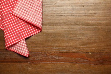 Photo of Red checkered tablecloth on wooden background, top view. Space for text