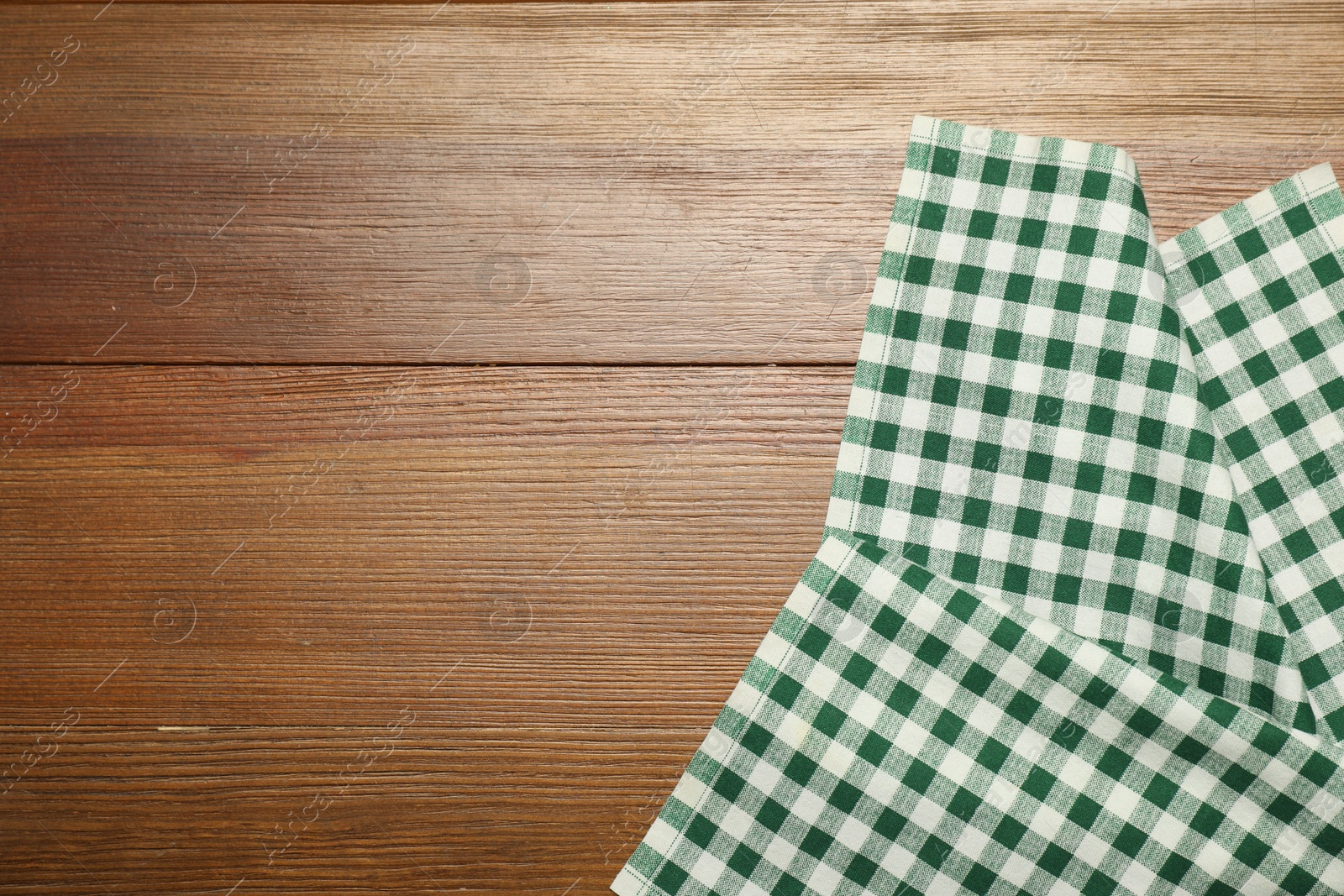 Photo of Green checkered tablecloth on wooden background, top view. Space for text