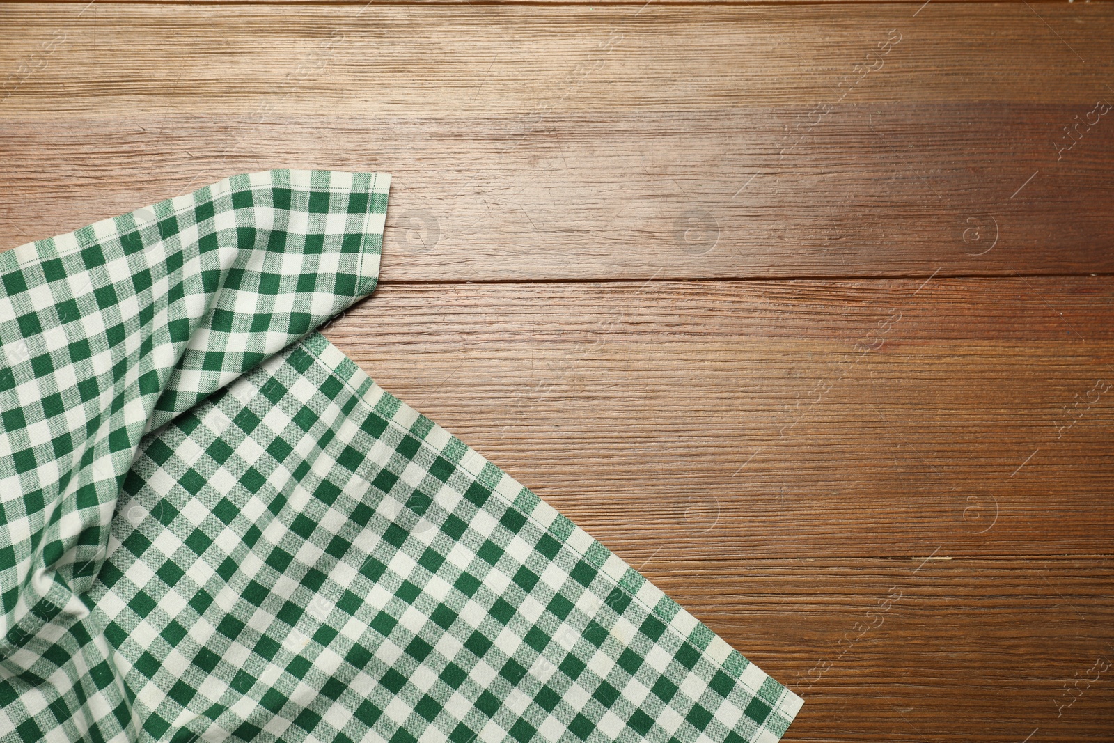 Photo of Green checkered tablecloth on wooden background, top view. Space for text