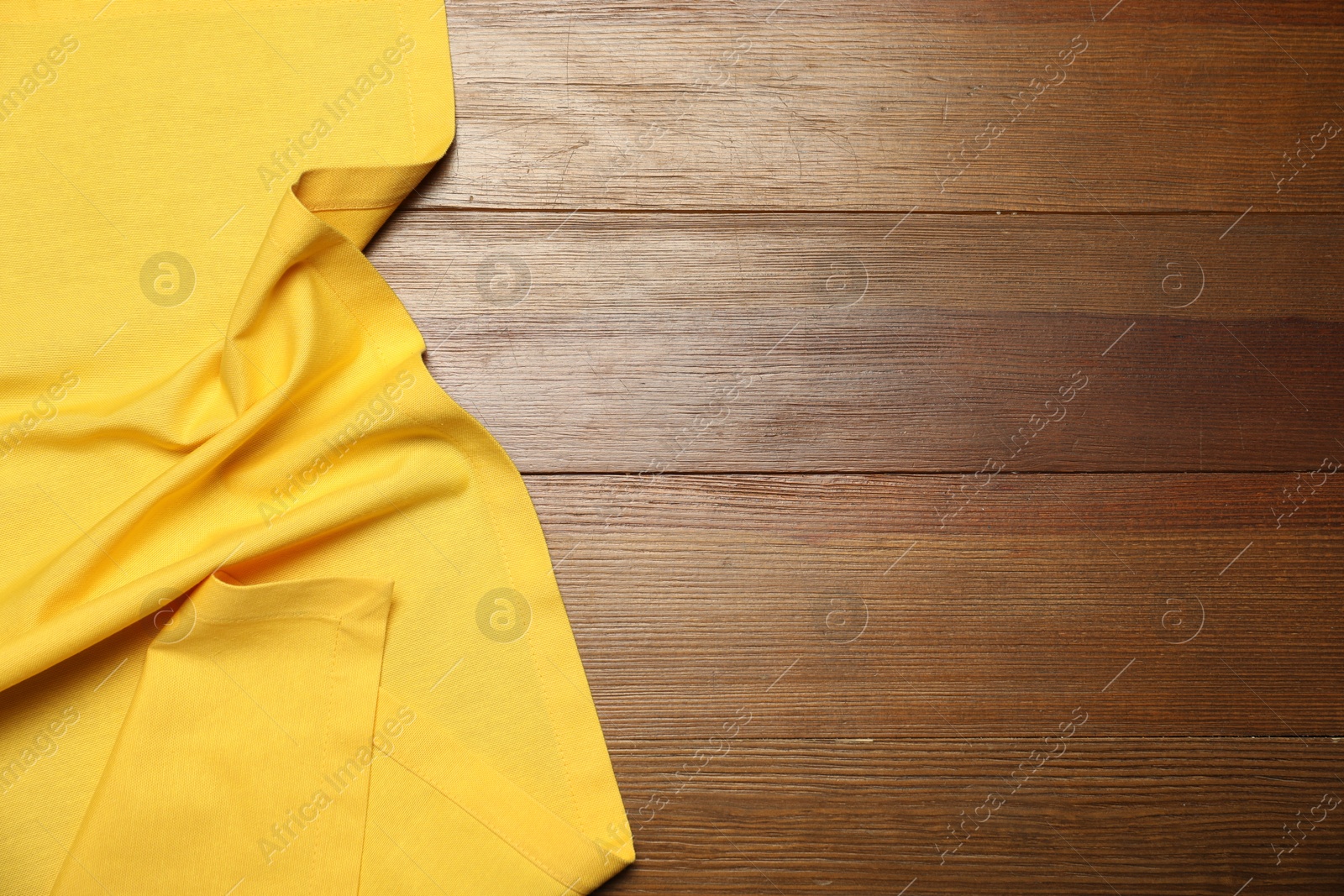 Photo of Yellow tablecloth on wooden background, top view. Space for text