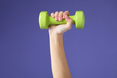 Photo of Woman exercising with dumbbell on purple background, closeup