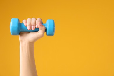 Photo of Woman exercising with dumbbell on orange background, closeup. Space for text