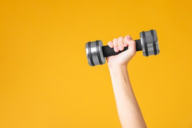 Photo of Woman exercising with dumbbell on orange background, closeup. Space for text