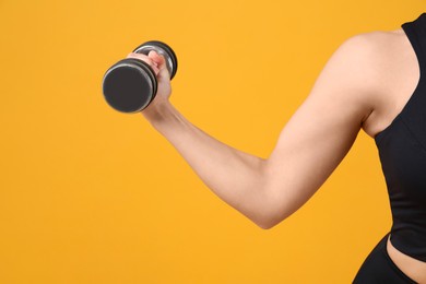 Photo of Woman exercising with dumbbell on orange background, closeup