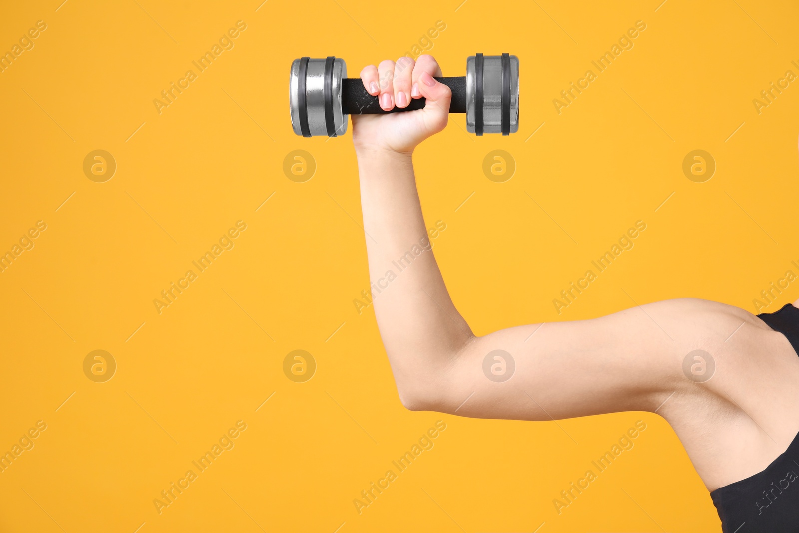 Photo of Woman exercising with dumbbell on orange background, closeup. Space for text