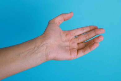 Photo of Woman with visible hand veins on light blue background, closeup