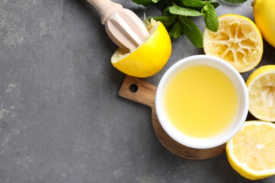 Photo of Fresh lemon juice in bowl, lemons, squeezer and mint on grey table, top view. Space for text