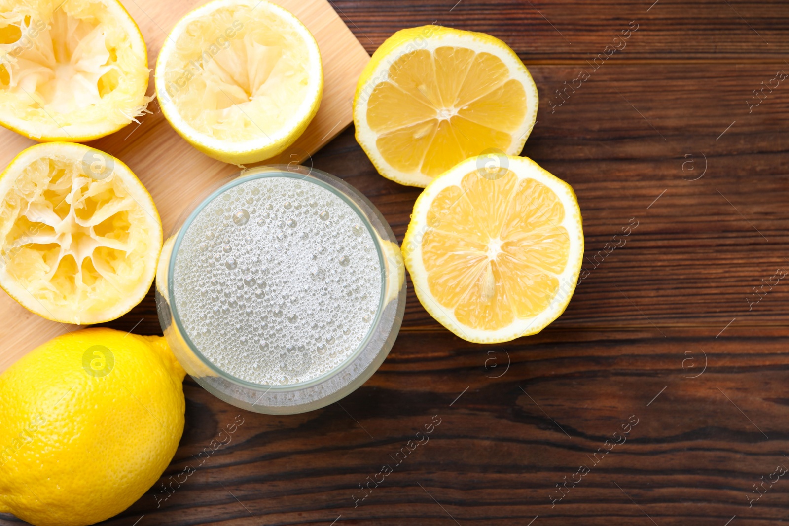 Photo of Fresh juice in glass and lemons on wooden table, top view