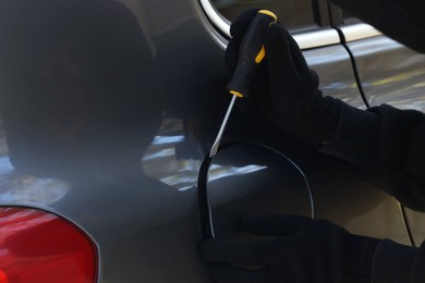 Photo of Thief with screwdriver opening fuel cap, closeup. Car hijacking