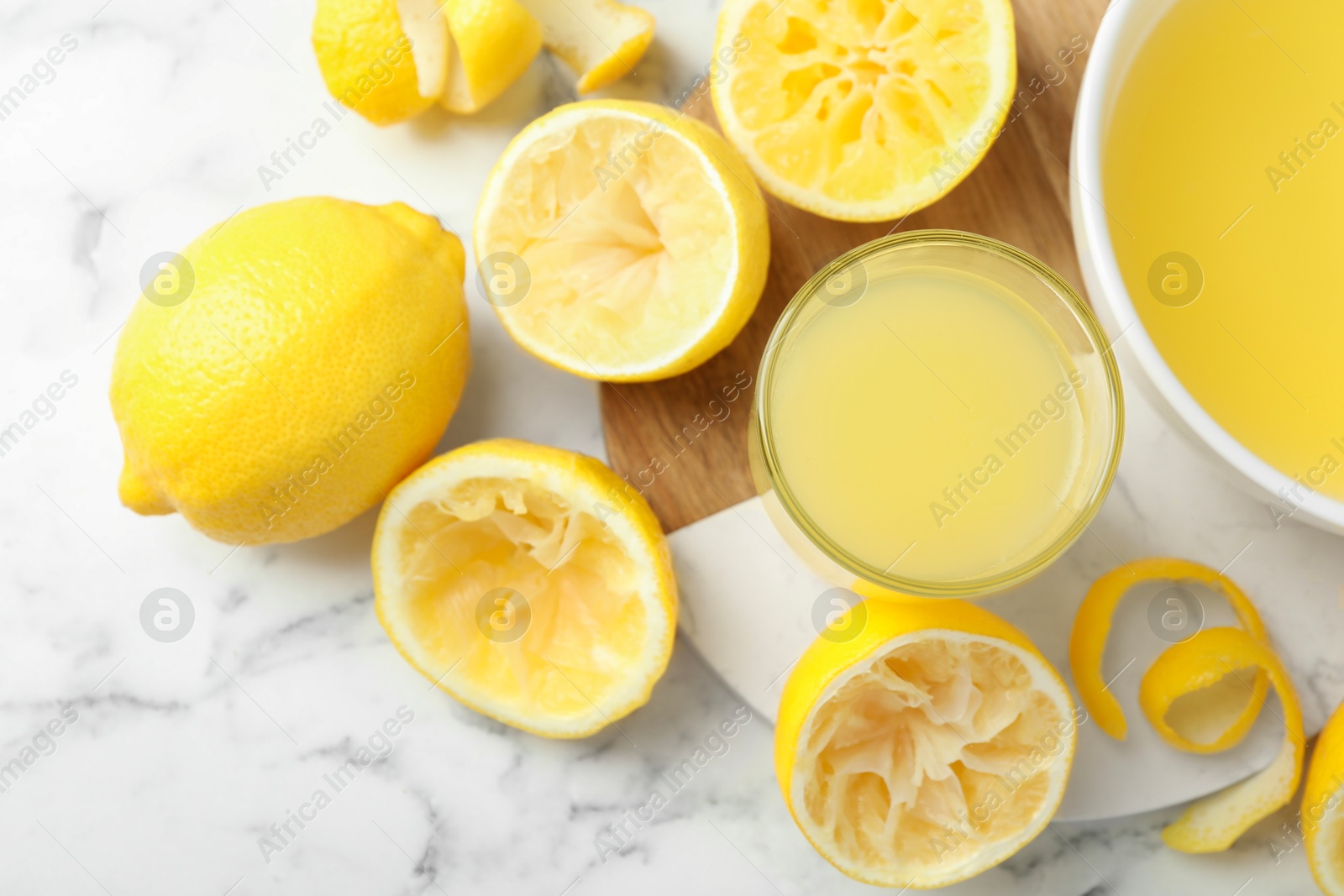 Photo of Fresh lemon juice and squeezed fruits on white marble table, flat lay