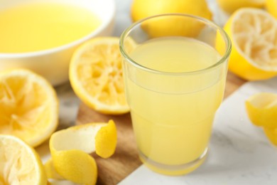 Photo of Glass of fresh lemon juice and squeezed fruits on table, closeup