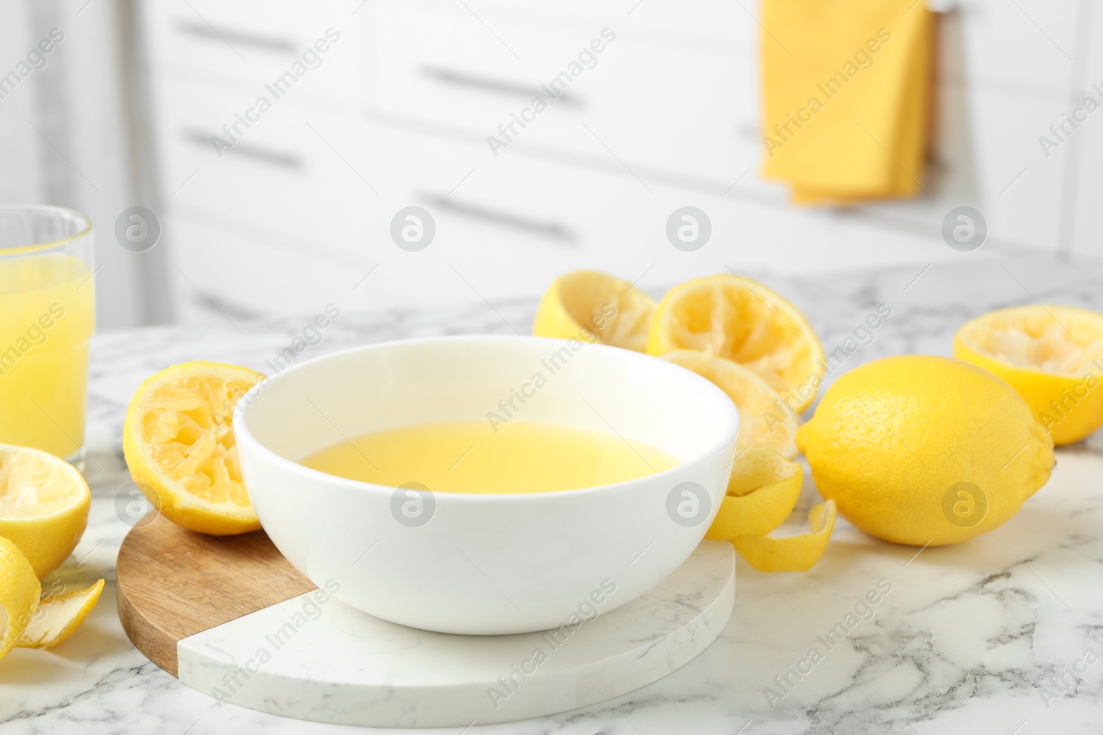 Photo of Bowl of fresh lemon juice and squeezed fruits on white marble table