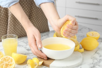 Photo of Woman squeezing lemon juice into bowl at marble table, closeup