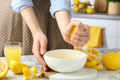 Photo of Woman squeezing lemon juice into bowl at marble table, closeup