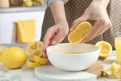 Photo of Woman squeezing lemon juice into bowl at marble table, closeup