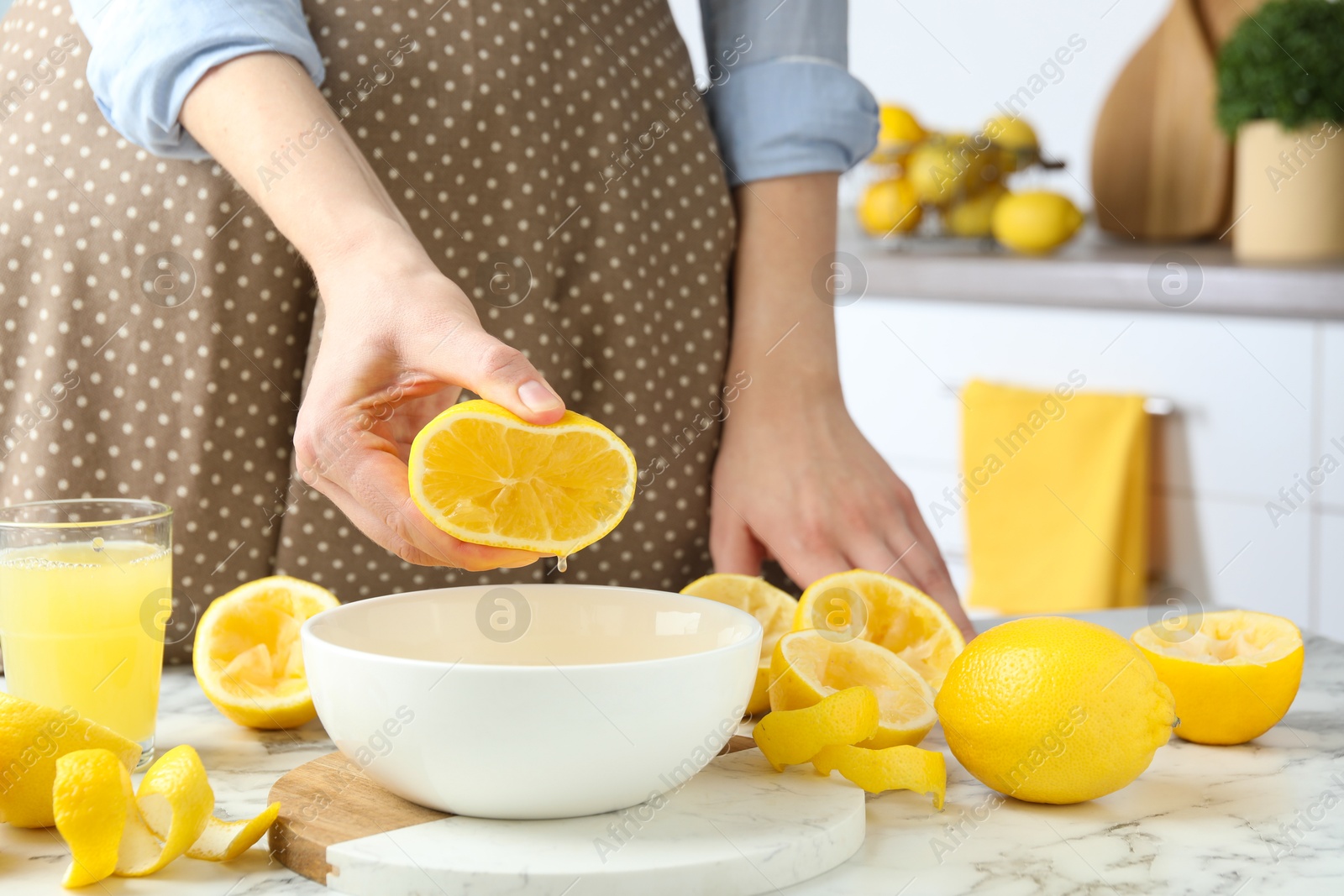 Photo of Woman squeezing lemon juice into bowl at marble table, closeup