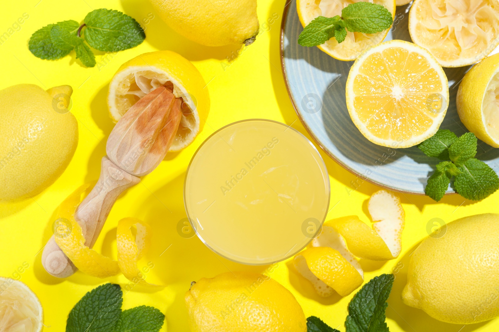 Photo of Glass of fresh lemon juice, squeezer and fruits on yellow background, flat lay