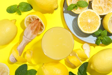 Photo of Glass of fresh lemon juice, squeezer and fruits on yellow background, flat lay