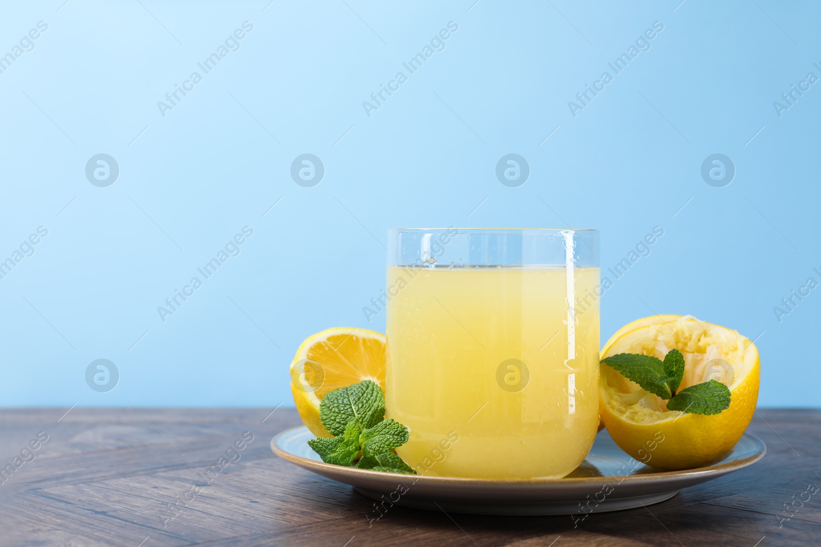 Photo of Glass of lemon juice and fresh fruits on wooden table. Space for text