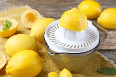 Photo of Juicer and fresh lemons on wooden table, closeup