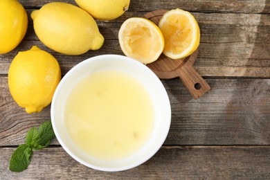 Photo of Fresh lemon juice in bowl and fruits on wooden table, flat lay