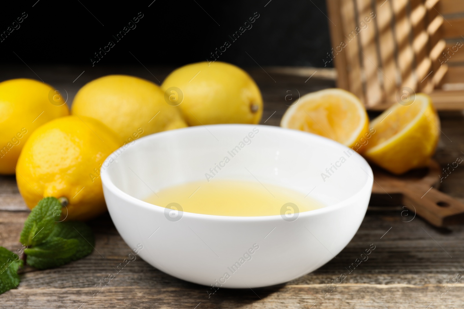 Photo of Fresh lemon juice in bowl and fruits on wooden table, closeup