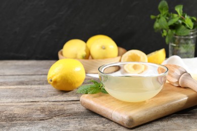 Photo of Fresh lemon juice in bowl, squeezer and fruits on wooden table