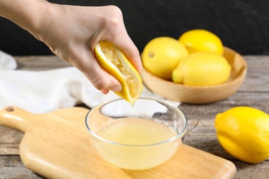 Photo of Woman squeezing lemon juice into bowl at wooden table, closeup