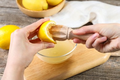 Photo of Woman juicing lemon into bowl at wooden table, closeup