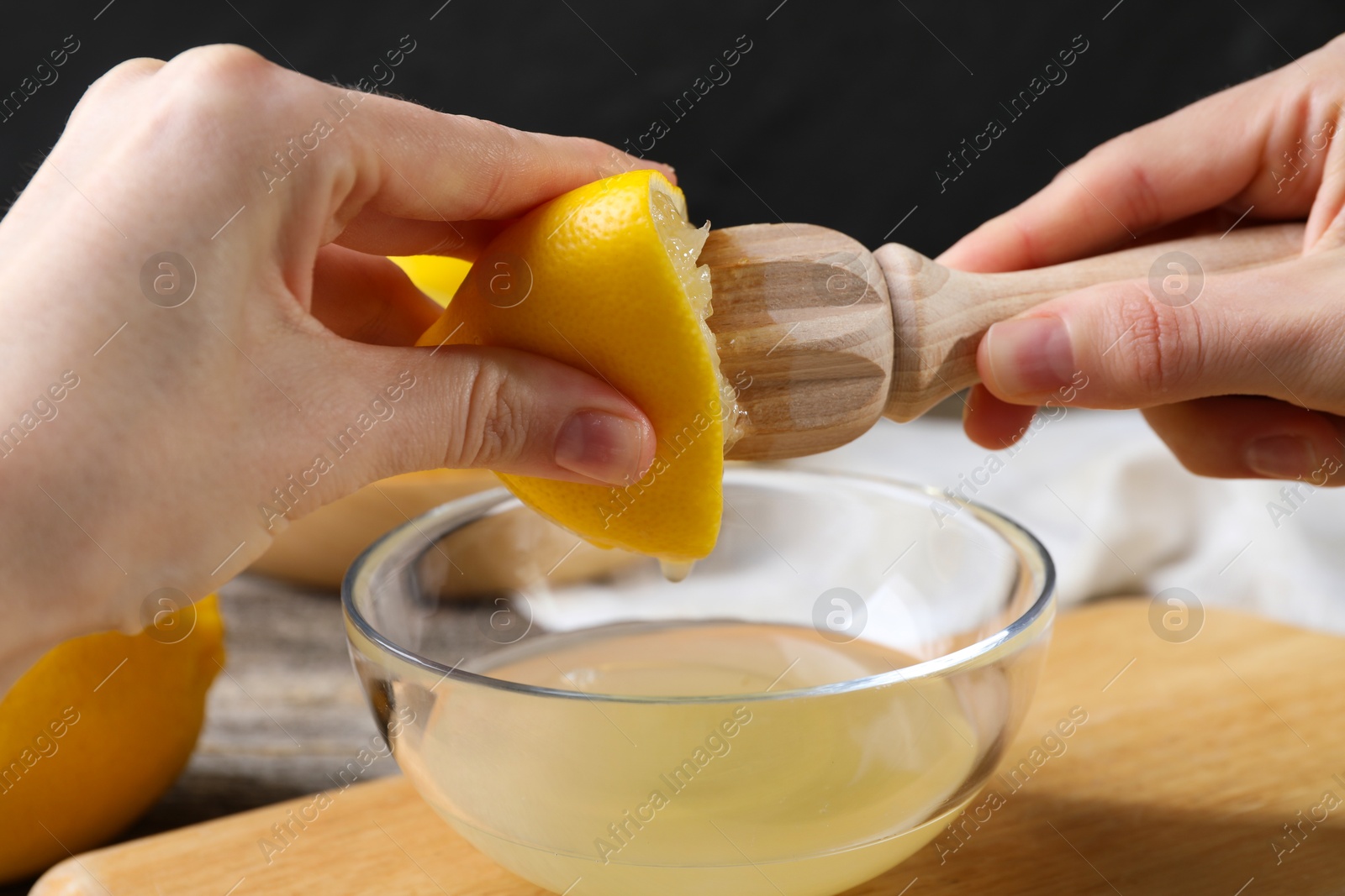 Photo of Woman juicing lemon into bowl at wooden table, closeup