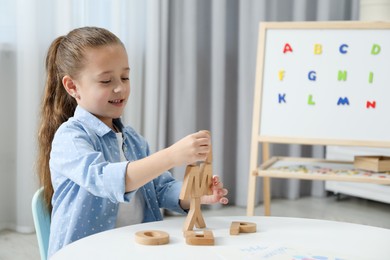 Photo of Little girl learning alphabet with wooden letters at white table indoors