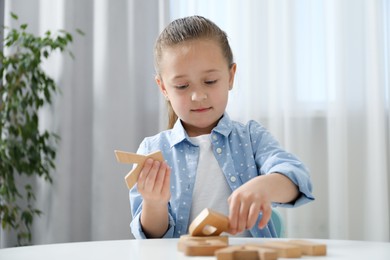 Photo of Little girl learning alphabet with wooden letters at white table indoors