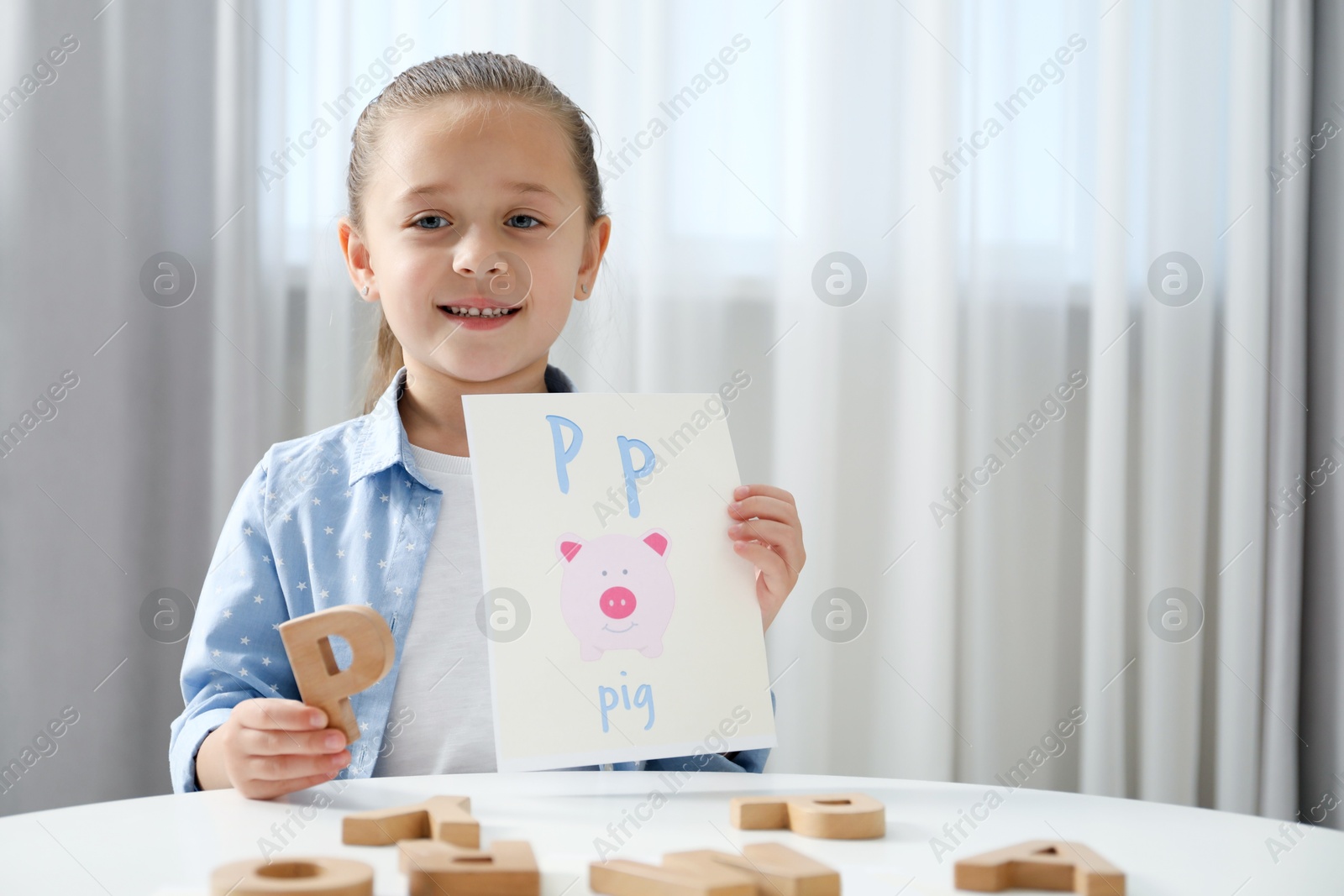 Photo of Learning alphabet. Little girl with wooden letter P and picture at white table indoors, space for text