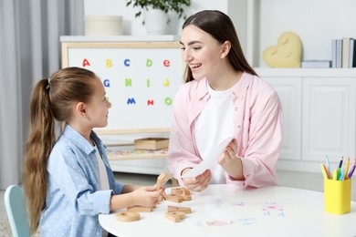 Speech therapist teaching little girl alphabet at white table indoors