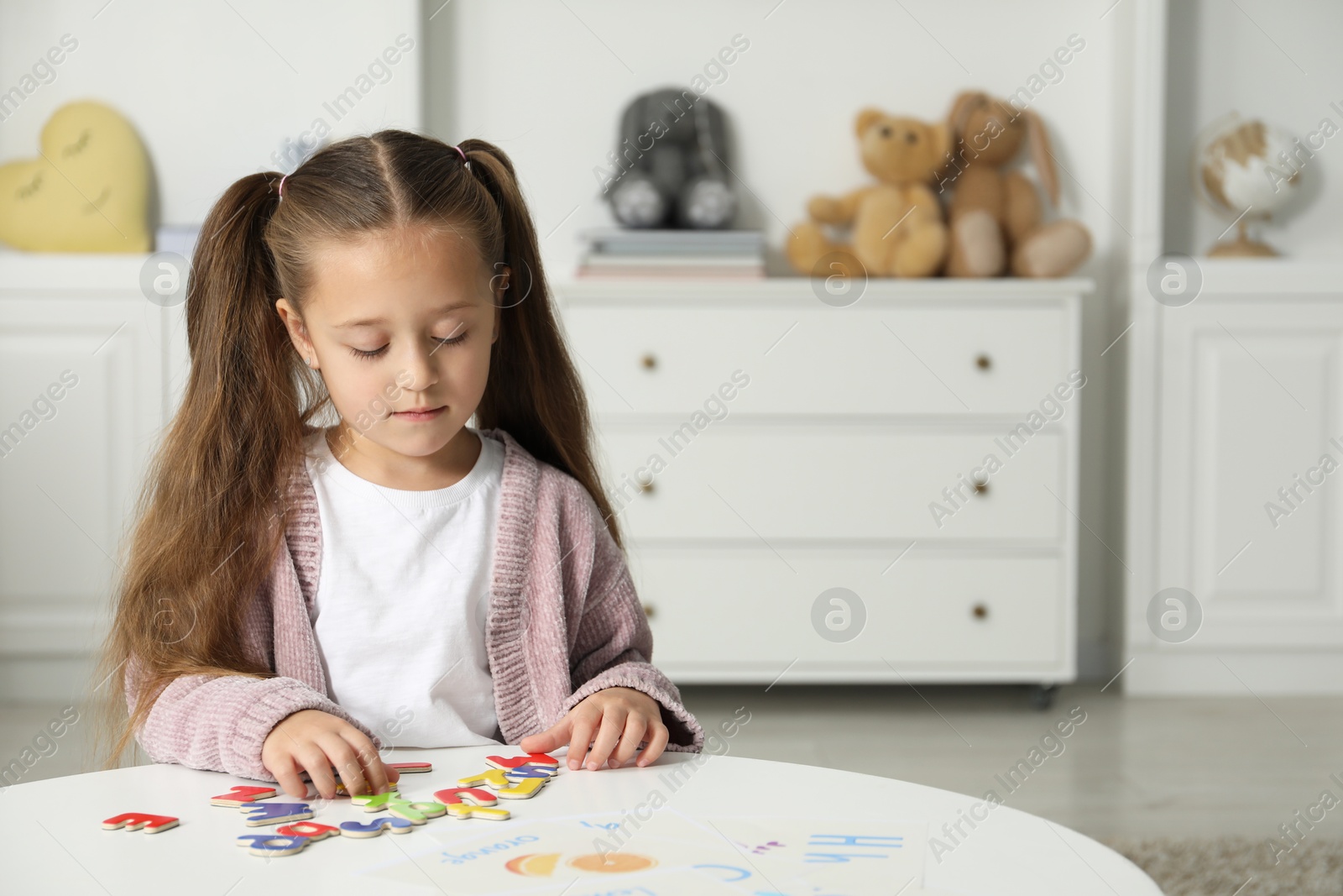 Photo of Little girl learning alphabet with magnetic letters at white table indoors, space for text