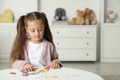 Photo of Little girl learning alphabet with magnetic letters at white table indoors, space for text