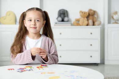 Photo of Little girl learning alphabet with magnetic letters at white table indoors, space for text