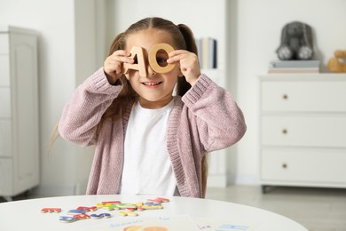 Photo of Little girl learning alphabet with different letters at white table indoors