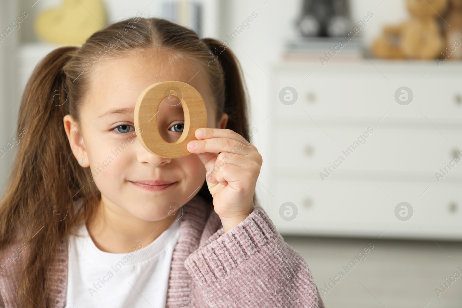 Photo of Learning alphabet. Little girl with wooden letter O indoors, space for text