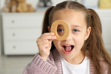 Photo of Learning alphabet. Little girl with wooden letter O indoors