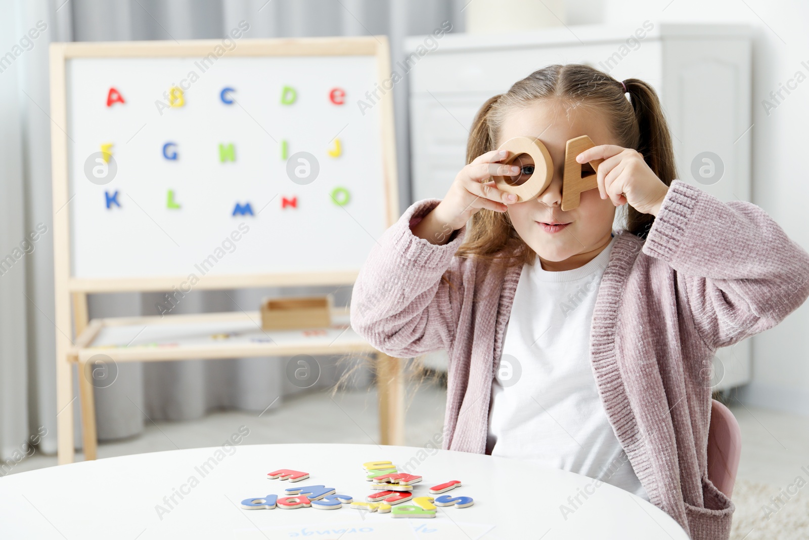 Photo of Little girl learning alphabet with different letters at white table indoors