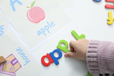 Photo of Little girl learning alphabet with different letters at white table indoors, above view