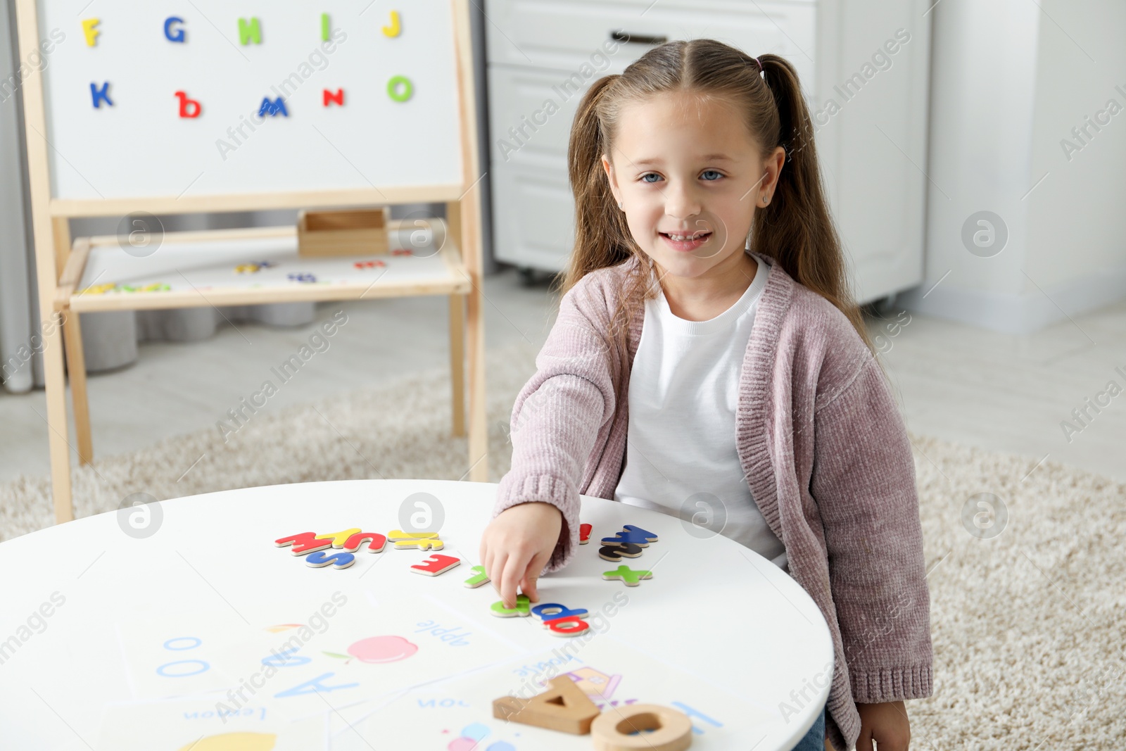 Photo of Little girl learning alphabet with different letters at white table indoors