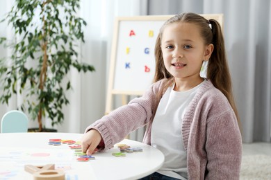 Photo of Little girl learning alphabet with different letters at white table indoors