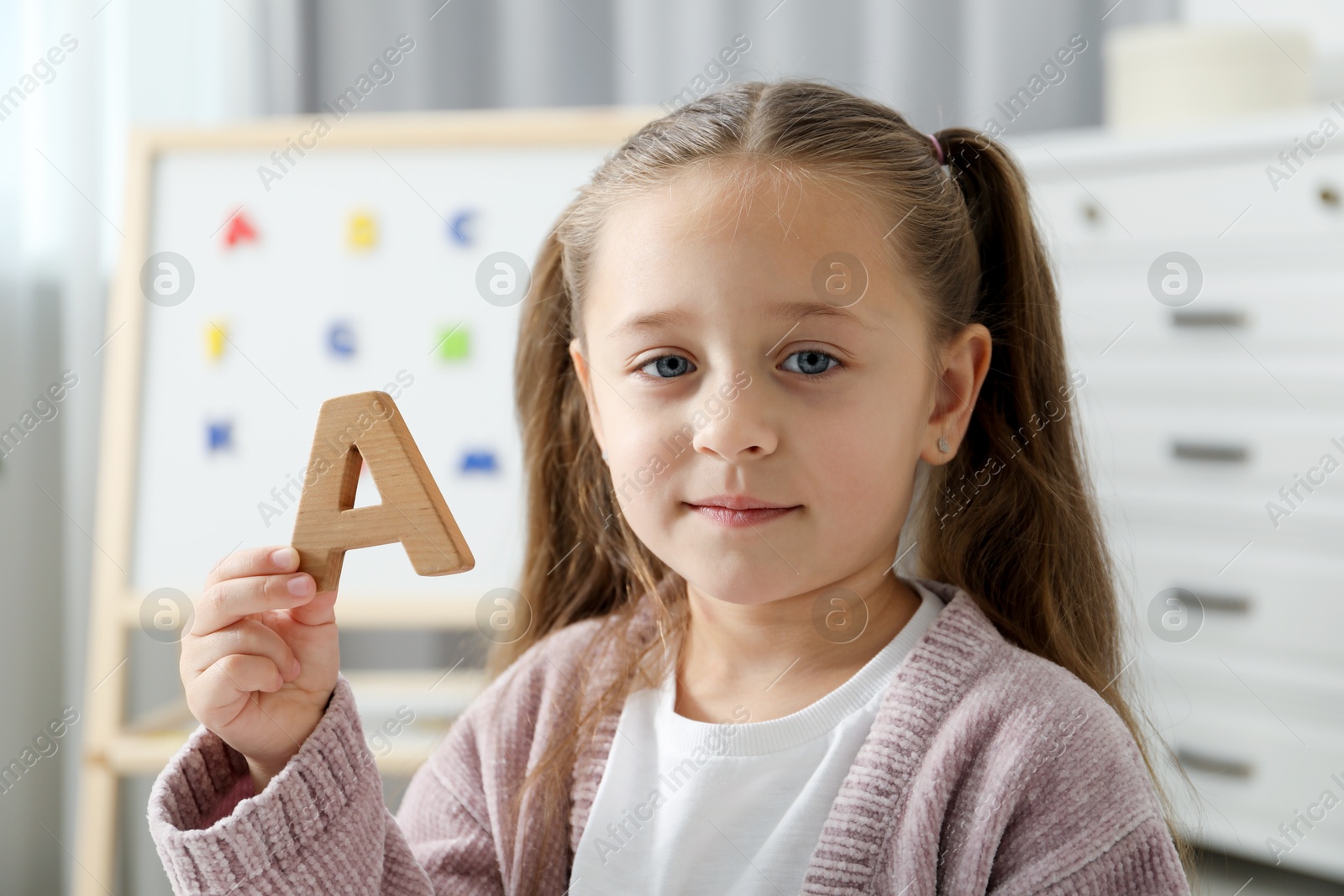 Photo of Learning alphabet. Little girl with wooden letter A indoors