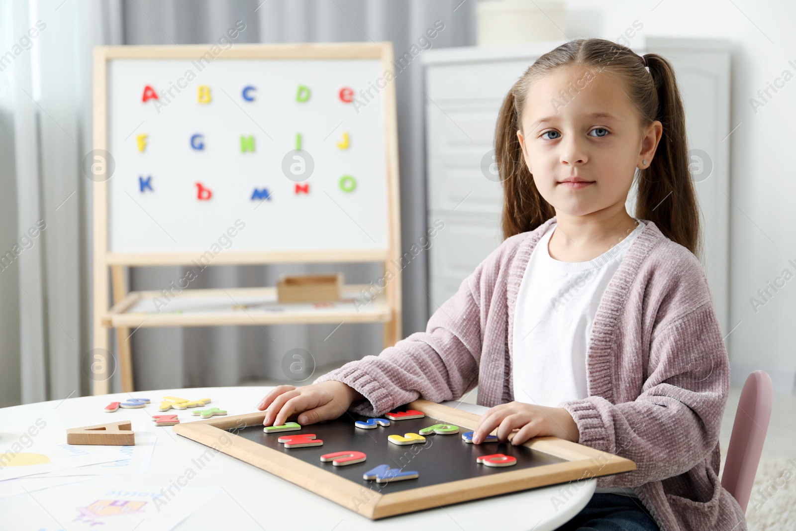 Photo of Little girl learning alphabet with magnetic letters at white table indoors