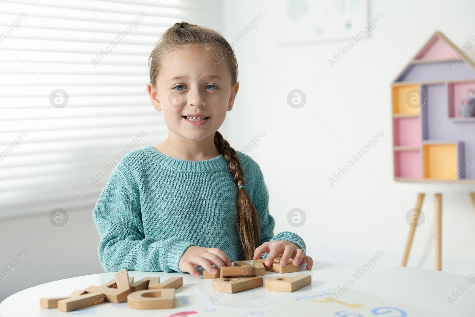 Photo of Little girl learning alphabet with wooden letters at white table indoors