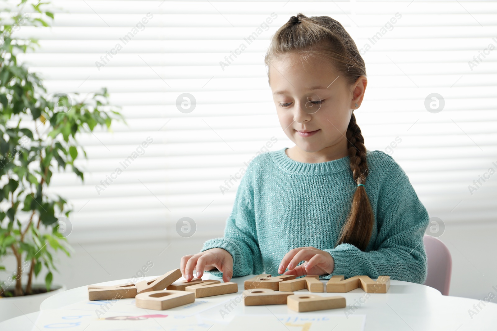 Photo of Little girl learning alphabet with wooden letters at white table indoors