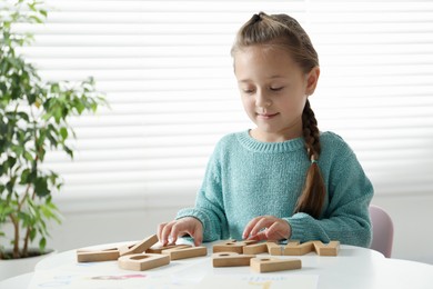 Photo of Little girl learning alphabet with wooden letters at white table indoors