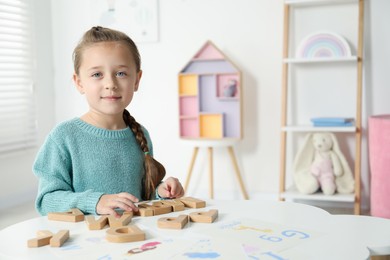 Photo of Little girl learning alphabet with wooden letters at white table indoors